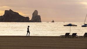 Une plage avec une personne qui se promène, des chaises longues et des parasols.