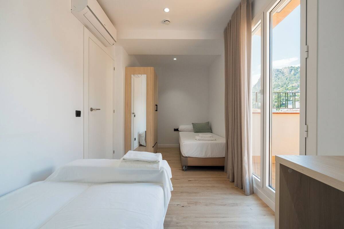 Een hotelkamer met een bed, een tafeltje, een raam met gordijnen en uitzicht op de omgeving.