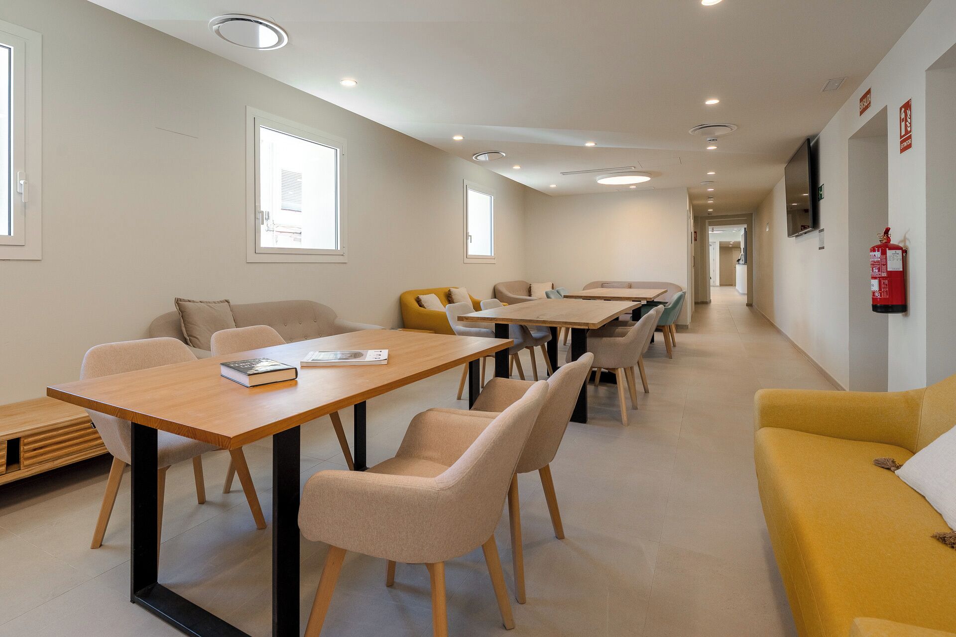 A modern hotel room with a long corridor, multiple seating areas, and a fire extinguisher on the wall.