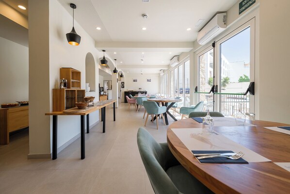 A modern restaurant with a long counter, multiple tables, and chairs. - Hotel Coral Boutique by gaiarooms (Torroella de Montgrí)