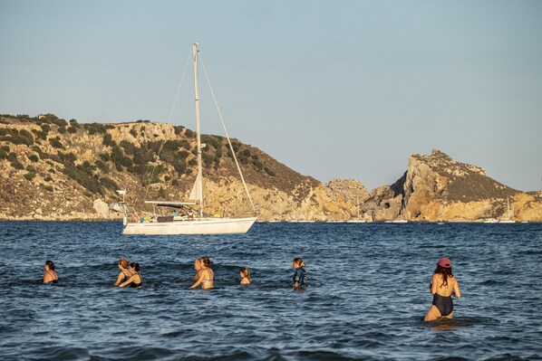 Paisaje costero con un velero y colinas rocosas al fondo.