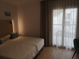 Ein Hotelzimmer mit zwei Betten, einem Kopfteil, einer Wandlampe und Blick durch transparente Vorhänge.