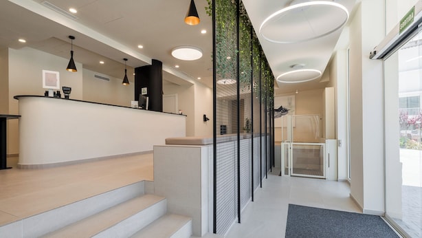 Un espace d’accueil avec un comptoir, des marches menant à une salle d’attente et une porte vitrée donnant accès à des toilettes.