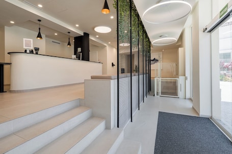A reception area with a counter, steps leading to a waiting area, and a glass door leading to a bathroom.. Hotel Coral Boutique by gaiarooms