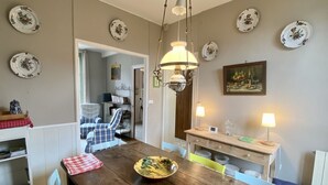 Uma sala de jantar com mesa de madeira, cadeiras e um lustre. Há pratos decorativos nas paredes e uma pintura acima da mesa.