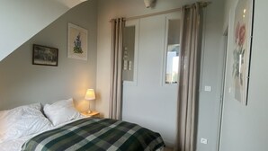Quarto com cama, mesa de cabeceira com luminária, janela com cortinas e obra de arte na parede.