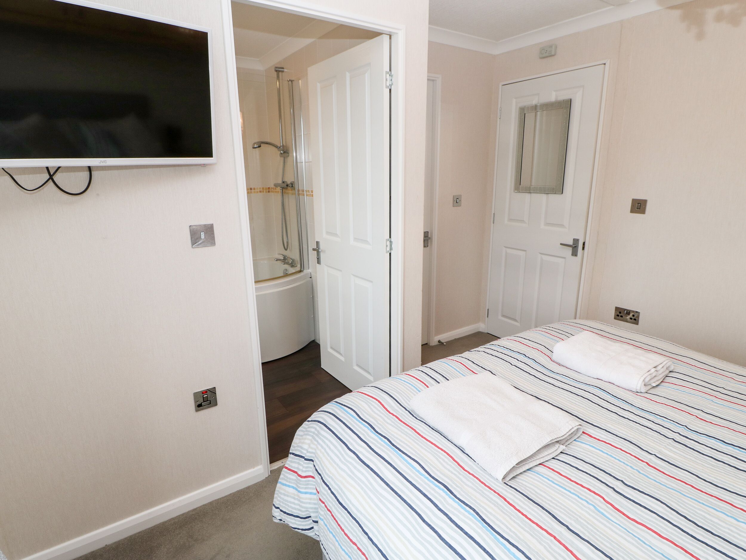 A bedroom with a bed, a TV mounted on the wall, a door leading to a bathroom, and a shower.