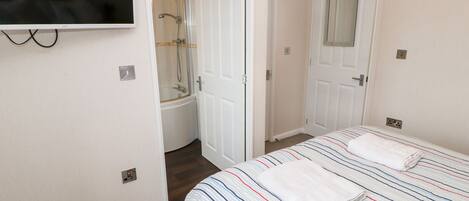 A bedroom with a bed, a TV mounted on the wall, a door leading to a bathroom, and a shower.