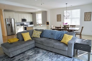 A modern living room with a grey sectional sofa, a small wooden side table, and a dining area with a wooden table and chairs. - Modern Midtown home with 3 king beds (Memphis)