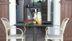 A dining table with two chairs, a bottle, a glass, and a flower arrangement. - Les parasols de madinina - Palm tree at the bungalow (Gros-Morne)
