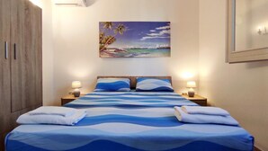 A hotel room with a bed, two bedside lamps, a painting of a beach scene, and a wardrobe. - Villa Piana - Con Piscina ed Ampio Giardino Privato (Tricase)