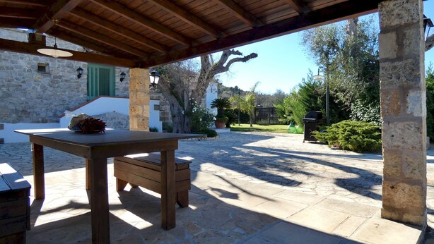 An outdoor patio with a wooden table and benches, stone flooring, and a stone wall. - Villa Piana - Con Piscina ed Ampio Giardino Privato (Tricase)