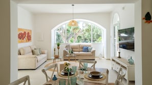 A dining area with a table set for four, surrounded by chairs, with a large window offering a view of trees and a white arched doorway. - Villa Machri - Con Piscina Privata E Ampio Giardino Vicina Al Mare (Alessano)