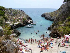 A crowded beach with rocky cliffs and clear blue water.