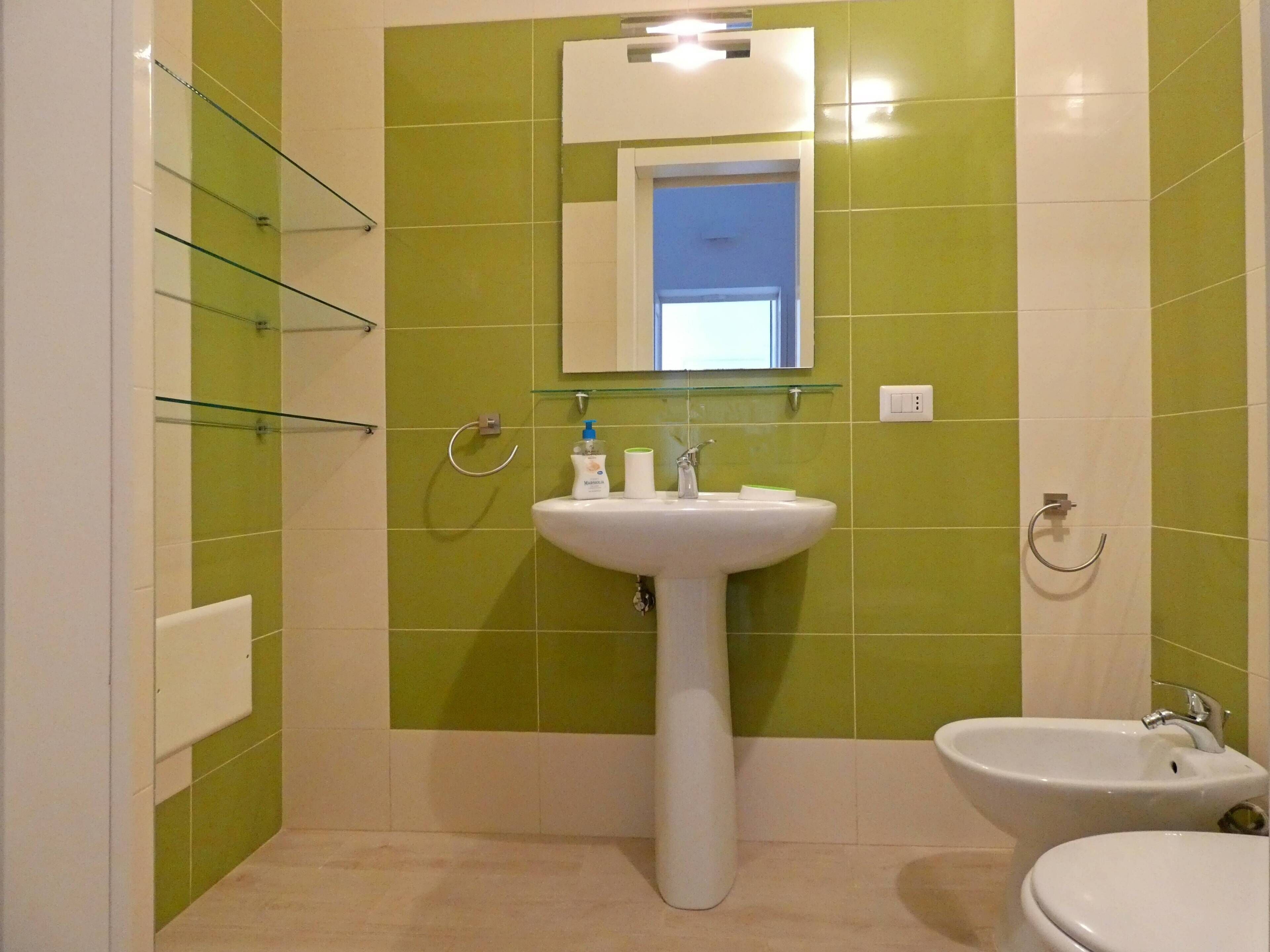 A bathroom with a white sink, a mirror above it, and a green-tiled wall.