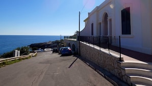 A coastal street with a white building, stone steps, and parked cars. - Corte del Mare - Dimora Fronte Mare nel Salento (Gagliano del Capo)