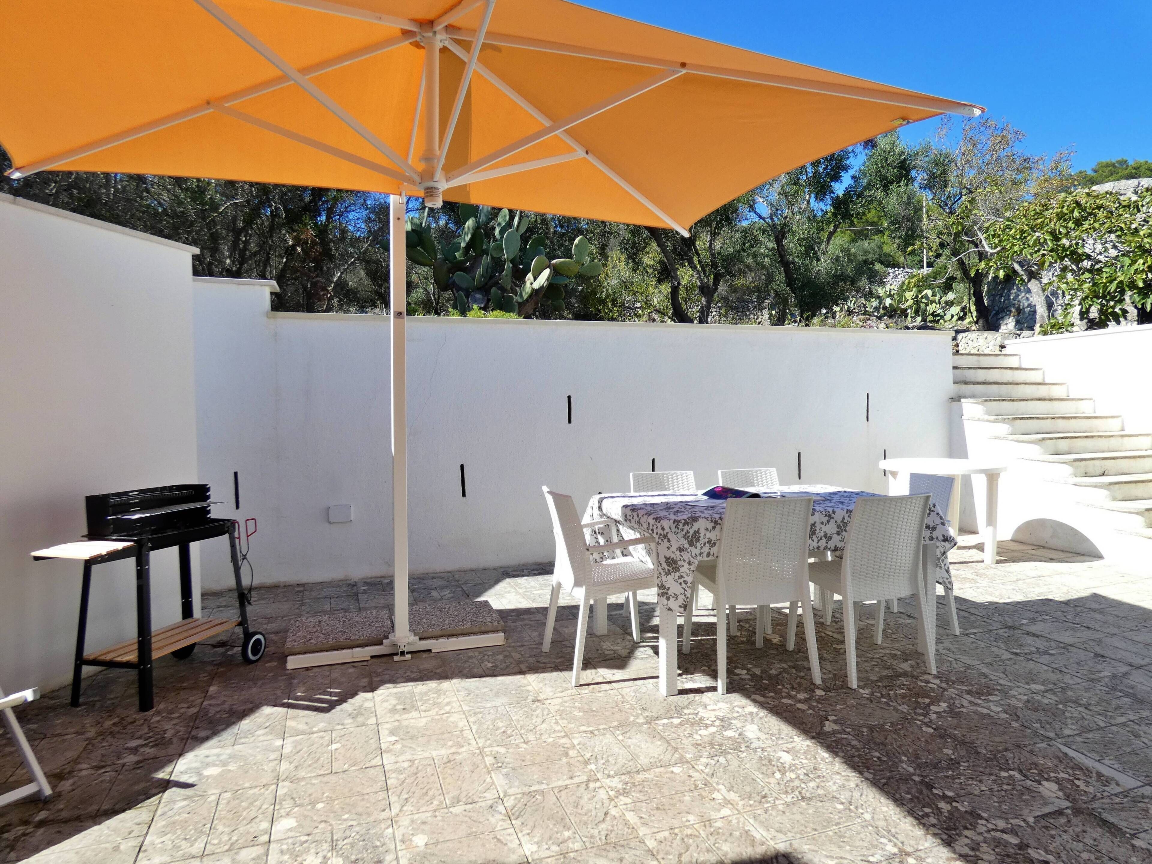 Une terrasse extérieure avec une table et des chaises, un parasol et un escalier menant à un niveau supérieur.