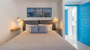 Una camera da letto con un letto, due quadri appesi al muro, lampade sui comodini e una porta blu.
