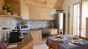 A kitchen with a microwave, stove, oven, and sink. There is a dining table set with plates and glasses. - Casa Celeste - Immersa Nella Natura con Piscina Privata nel Salento (Corsano)