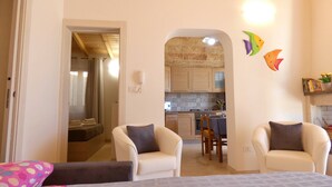 A cozy living room with two armchairs, a dining table, and a kitchen visible through an archway. - Casa Celeste - Immersa Nella Natura con Piscina Privata nel Salento (Corsano)