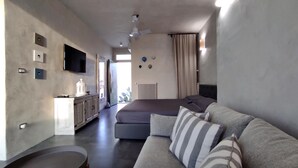 A modern hotel room with a sofa, a television, a ceiling fan, and a view of the outdoors.