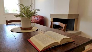 A wooden table with a potted plant, an open book, and a fireplace in the background.