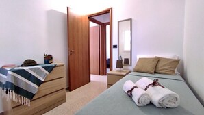 A bedroom with a bed, bedside table, and a wardrobe. There is a door leading to another room.