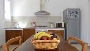 A kitchen with a wooden table, a wicker fruit basket, a microwave, and a refrigerator.