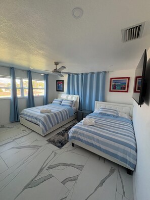 A bedroom with two beds, a ceiling fan, a window with curtains, and a mounted TV.