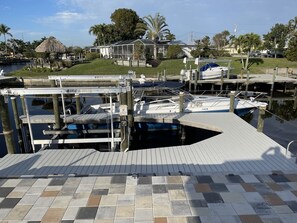 Un puerto deportivo con barcos amarrados, un elevador de embarcaciones y una casa al fondo.