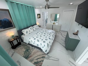 A bedroom with a bed, bedside table, lamp, dresser, mirror, and a TV mounted on the wall. - Ultimate Gulf Getaway: Kayaks, Jet Skis and Tours (Cape Coral)