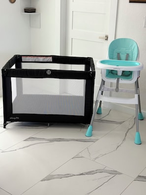 A baby playpen and a high chair in a room with a tiled floor and a white door. - Ultimate Gulf Getaway: Kayaks, Jet Skis and Tours (Cape Coral)