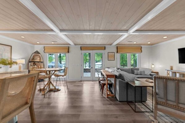 A spacious living area with a wooden ceiling, a sofa, a dining table, and a TV mounted on the wall.