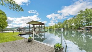 Un área de piscina al aire libre tranquila, con una zona de estar cubierta, un muelle y macetas con plantas.