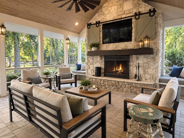 A stone fireplace with a flat-screen TV above it, surrounded by seating and a ceiling fan. - 726 Halfmoon Shores Drive · 6BR Lake Front - Boathouse - Dock - Screened Porch (Ten Mile)