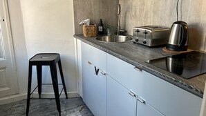 A compact kitchen with a sink, toaster, kettle, and a stool.