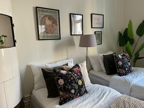 A hotel room with two beds, a large potted plant, and framed artwork on the wall.