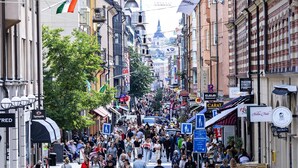 A busy urban street with pedestrians, shops, and various signs.