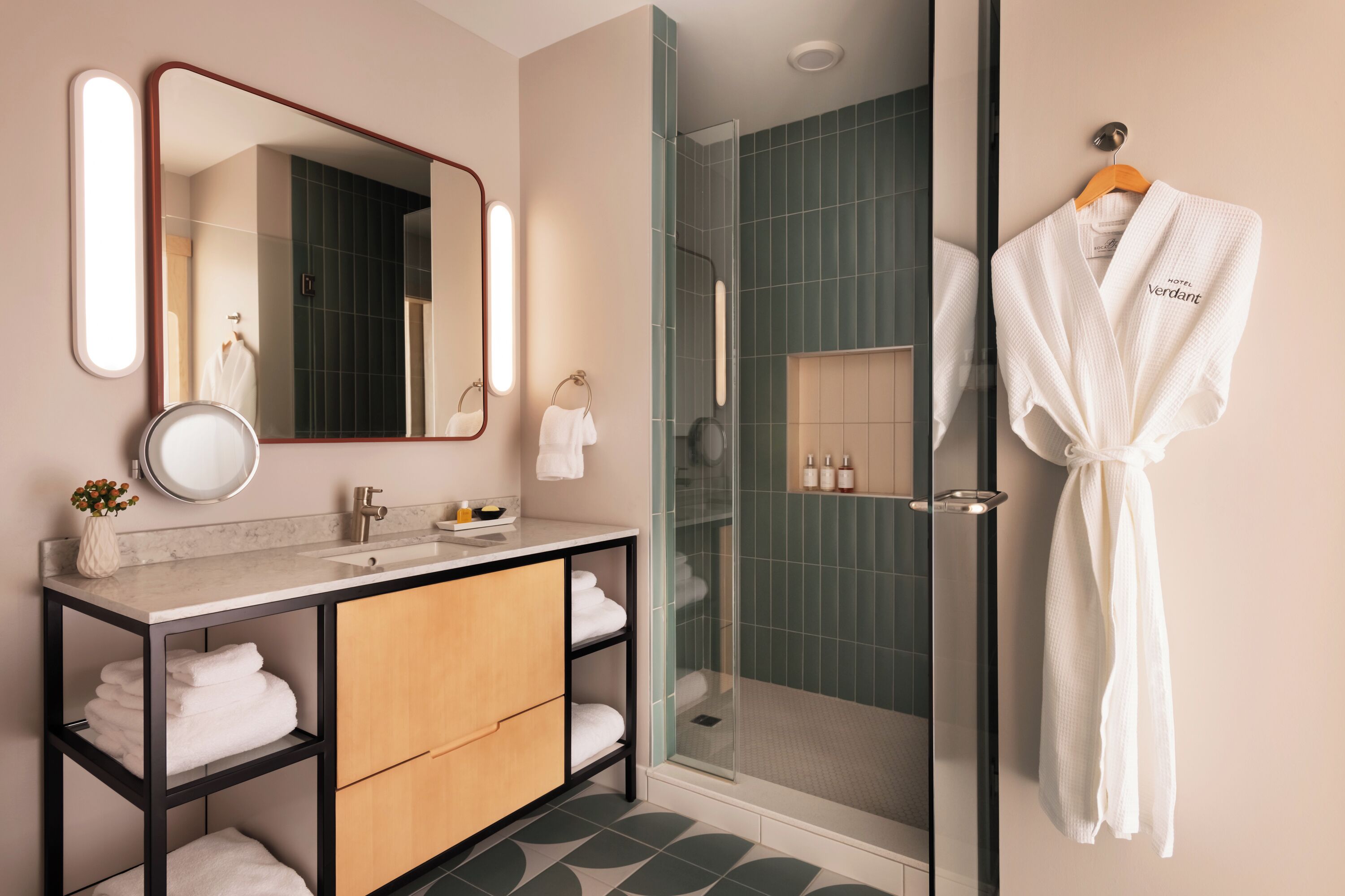 A modern bathroom with a glass shower enclosure, a vanity with a mirror, and a robe hanging on the wall.