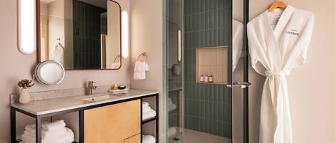 A modern bathroom with a glass shower enclosure, a vanity with a mirror, and a robe hanging on the wall.