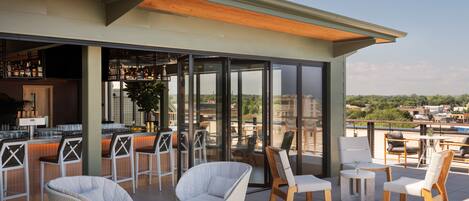 A rooftop bar with outdoor seating, including wicker chairs and tables, and a view of the cityscape.
