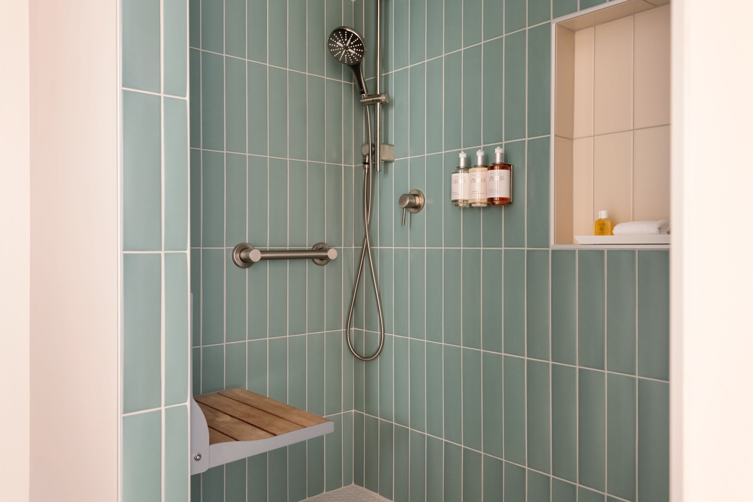 Une salle de bain avec des carreaux de couleur turquoise, une pomme de douche, une étagère en bois et une petite étagère contenant des articles de toilette.