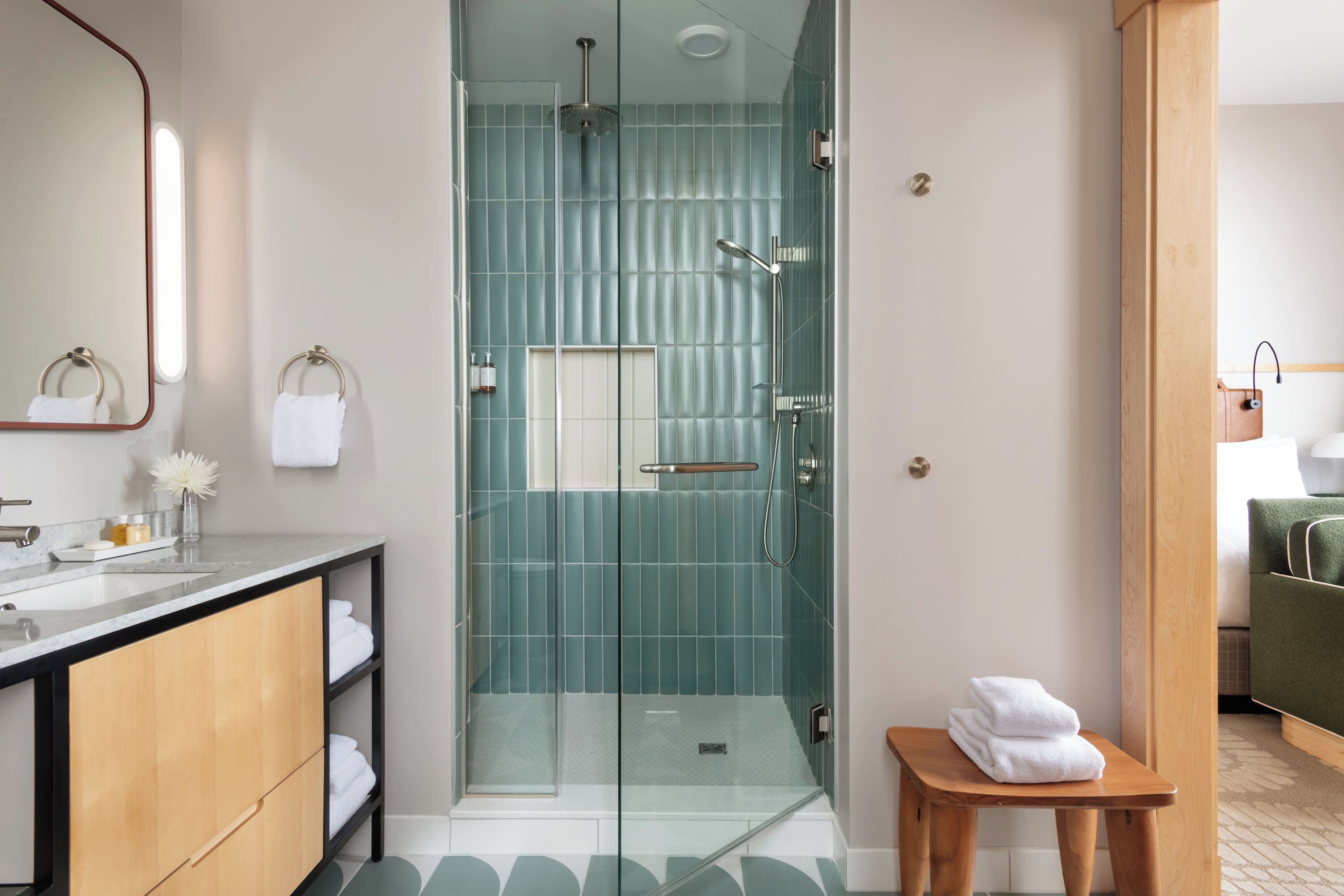 Een moderne badkamer met een glazen douchecabine, een houten wastafelmeubel en een klein tafeltje met handdoeken.