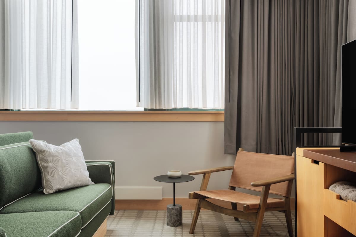 A modern room with a green sofa, a wooden chair, a small round table, and a TV on a wooden stand.
