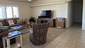 A living room with a sofa, coffee table, patterned armchair, TV, and a ceiling fan. - Beautiful desert house! (Yuma)