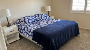 A bedroom with a bed, two bedside tables, a lamp on each table, a window with blinds, and a carpeted floor. - Beautiful desert house! (Yuma)