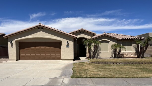 A residential house with a large garage, a well-maintained lawn, and a clear blue sky. - Beautiful desert house! (Yuma)