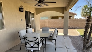 An outdoor patio with a table and chairs, a ceiling fan, and a view of a brick wall and palm tree. - Beautiful desert house! (Yuma)