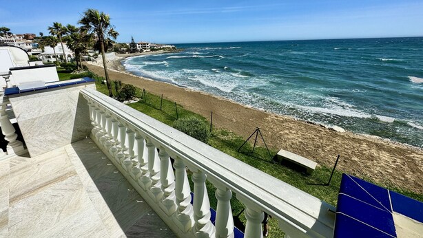 Une vue sur la côte depuis un balcon doté d’une balustrade blanche, avec une plage de sable et l’océan en toile de fond.