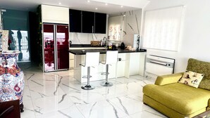 Une cuisine moderne avec un sol en marbre, un îlot central doté de tabourets de bar et un canapé jaune dans l’espace salon.